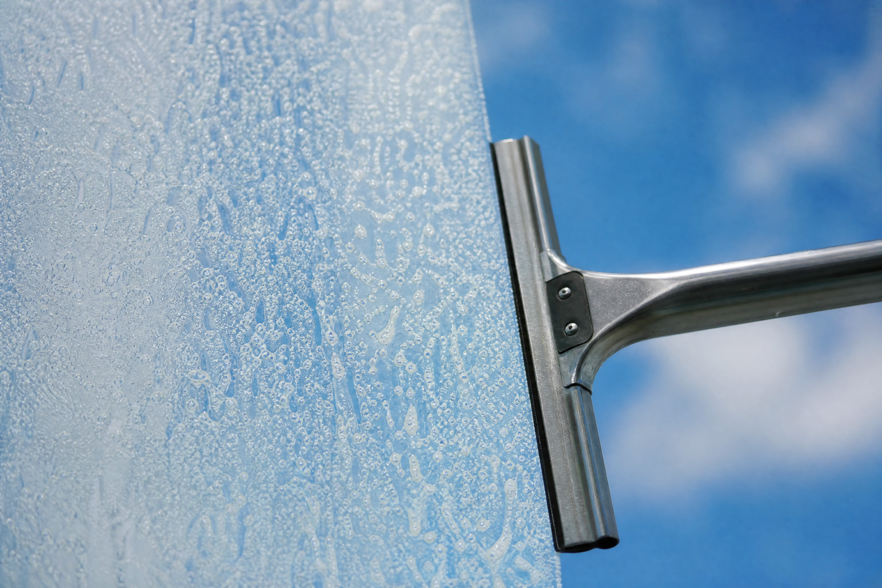 Wisser haalt zeepwater van een ruit: links nog schuim, rechts glashelder glas met blauwe lucht